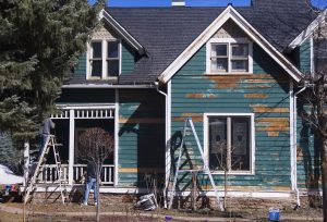 A house with wood lap siding is in the process of being painted.
