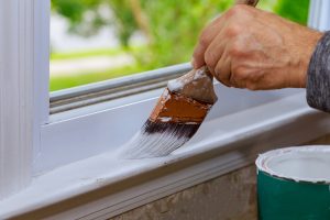 A hand is shown applying wait paint to an interior windowsill.