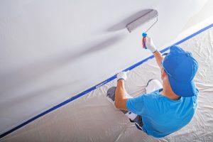 A man wearing a cap applies paint on wall